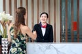Happy smiling young beautiful Asian female receptionist in suit shaking hands with customer at hotel reception counter desk, check Royalty Free Stock Photo