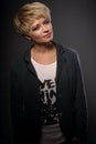 Happy smiling young blond woman with short bob hair style looking in grey trendy jacket on dark background. Closeup Royalty Free Stock Photo