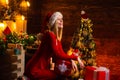 Happy smiling young blonde woman in red dress and Santa`s hat at Christmas decorated background. Celebrating Christmas