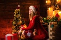 Happy smiling young blonde woman in red dress and Santa& x27;s hat at Christmas decorated background. Celebrating