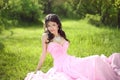 Happy smiling young bride girl dreaming and resting on green grass at spring park. Attractive brunette model wearing in pink Royalty Free Stock Photo