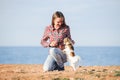 Happy smiling young caucasian woman in plaid shirt and jeans playing with her small pet chihuahua dog on sea shore Royalty Free Stock Photo