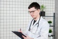 Happy smiling young doctor writing on clipboard in a modern hospital Royalty Free Stock Photo