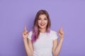 Happy smiling young female wearing white casual t shirt pointing both index fingers up, showing free space for advertisement or Royalty Free Stock Photo