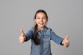happy smiling young girl in casual clothes looking at camera and showing thumbs up, isolated on grey background Royalty Free Stock Photo
