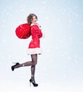 Happy smiling young girl in Santa Claus costume holds red big bag of gifts on a light blue background with snow. Royalty Free Stock Photo