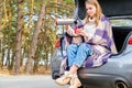 Happy smiling young girl sitting in the trunk of a car pours hot tea into a cup of thermos against the backdrop of a Royalty Free Stock Photo