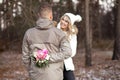 Happy smiling young couple in casual upper garments stand meeting eyes while man hiding bouquet of white, pink flowers. Royalty Free Stock Photo