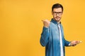 Happy smiling young man in casual standing and using tablet computer isolated over yellow background. Pointing finger away Royalty Free Stock Photo