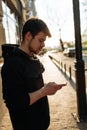 Happy smiling young man using modern smart phone while standing at crosswalk at the sunset in city center Royalty Free Stock Photo