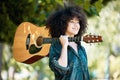 Happy smiling young mixed race female musician holding her guitar while standing snd enjoying a relaxing day in the park