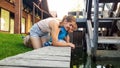 Portrait of happy smiling young mother with her little toddler son touching water in canal next toold wooden water mill