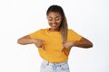 Happy smiling young woman, black girl pointing fingers down and looking at promo text, showing copy space, standing over Royalty Free Stock Photo