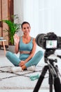 Happy smiling young woman blogger with camera on tripod recording online yoga class at home Royalty Free Stock Photo