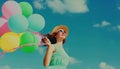 Happy smiling young woman with bunch of colorful balloons wearing a summer straw hat on the field on blue sky background Royalty Free Stock Photo