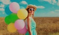 Happy smiling young woman with bunch colorful balloons wearing a summer straw hat on the field on a blue sky background Royalty Free Stock Photo