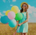 Happy smiling young woman with bunch of colorful balloons wearing a summer straw hat on the field on blue sky background Royalty Free Stock Photo