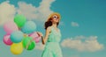 Happy smiling young woman with bunch of colorful balloons wearing a summer straw hat on the field on blue sky background Royalty Free Stock Photo