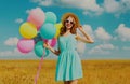 Happy smiling young woman with bunch colorful balloons wearing a summer straw hat on the field on a blue sky background Royalty Free Stock Photo