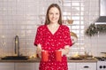 Happy smiling young woman holding or carrying two cups or mugs of tea at kitchen at christmas time Royalty Free Stock Photo