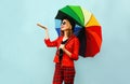 Happy smiling young woman holding colorful umbrella, checking with outstretched hand rain, wearing red jacket, black hat on blue Royalty Free Stock Photo