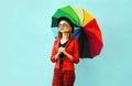 Happy smiling young woman holding colorful umbrella in hands, wearing red jacket, black hat Royalty Free Stock Photo