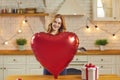 Smiling young woman holding big heart-shaped balloon standing in the kitchen on Valentine`s Day Royalty Free Stock Photo