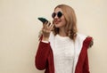 Happy smiling young woman holding smartphone using voice command recorder, assistant or takes calling wearing red jacket