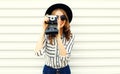 Happy smiling young woman holding vintage film camera in black round hat, shorts, white striped shirt on white wall Royalty Free Stock Photo