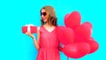 Happy smiling young woman holds gift box with pink heart shaped air balloons on colorful blue Royalty Free Stock Photo