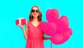 Happy smiling young woman holds gift box with pink heart shaped air balloons on colorful blue Royalty Free Stock Photo