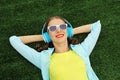 Happy smiling young woman listening to music in headphones while lying on grass in summer park Royalty Free Stock Photo