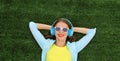 Happy smiling young woman listening to music in headphones while lying on grass in summer park Royalty Free Stock Photo