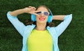 Happy smiling young woman listening to music in headphones while lying on grass in summer park Royalty Free Stock Photo