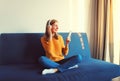 Happy smiling young woman listening to music with wireless headphones looking at smartphone sitting on the couch at home Royalty Free Stock Photo