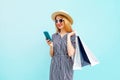 Happy smiling young woman with phone, holding colorful shopping bags in summer round straw hat, striped dress on blue Royalty Free Stock Photo