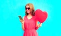 Happy smiling young woman with phone, pink heart shaped air balloons on colorful blue Royalty Free Stock Photo