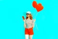 Happy smiling young woman with phone, red heart shaped air balloons in summer straw hat and shorts Royalty Free Stock Photo