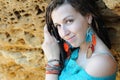 Happy smiling young woman portrait with dreadlocks hairstyle posing near yellow stone rock, dressed in leather feather earrings Royalty Free Stock Photo