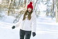 Happy smiling young woman in red hat standing in snowy forest. Portrait of a young girl in sunny day in winter park