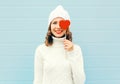 Happy smiling young woman with red lips holds lollipop heart wearing knitted hat sweater over blue Royalty Free Stock Photo