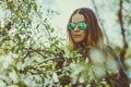 Happy smiling young woman in sunglasses and a knitted jacket enjoying spring flowers in the garden Royalty Free Stock Photo