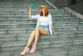 Happy smiling young woman taking selfie picture by smartphone sitting on the stairs on city street