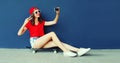Happy smiling young woman taking selfie with smartphone sitting on skateboard wearing red baseball cap, shorts on city street on Royalty Free Stock Photo