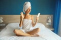 Happy smiling young woman is on video call with smartphone and waving hand or taking selfie drying her wet hair after bath with Royalty Free Stock Photo