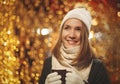 Happy smiling young woman in winter clothes holding cup with christmas lights in background Royalty Free Stock Photo