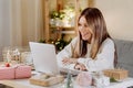 Happy and smiling young woman wrapping and preparing Christmas gifts, typing at laptop and having online video chat Royalty Free Stock Photo