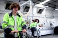 Happy smiling young worker man with curly hair wearing glasses and safety vest working in factory, industrial male engineer Royalty Free Stock Photo