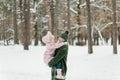 Happy and smilling young mother and her little daughter spending time together, outside in winter forest