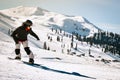 Happy snowboarder dressed in dark black sportswear riding down the mountain slope in Georgia, Goderdzi on caucasus sunny day